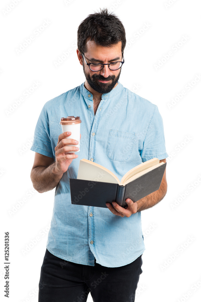 Handsome man with blue glasses reading book and drinking coffee Handsome man with blue glasses reading book and drinking coffee