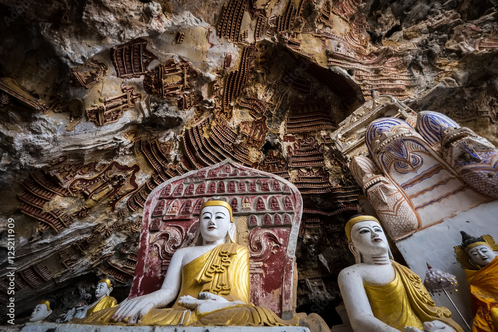 Fototapeta premium Amazing view of lot Buddhas statues and religious carving on limestone rock in sacred Kaw Goon cave. Hpa-An, Myanmar (Burma) travel landscapes and destinations