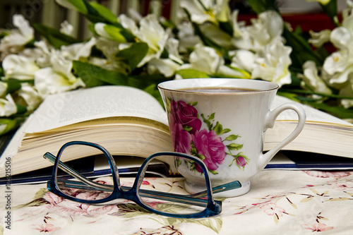 Concept image with open book, coffee cup, reading glasses with flowers in background. photo