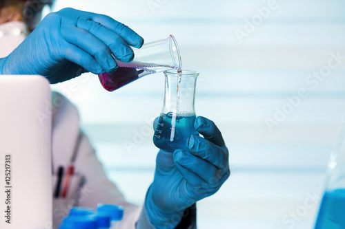 Wall Mural chemist working in laboratory mixing fluids / scientist holding tubes test in th