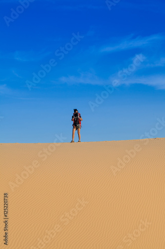 Female photographer with her backpack travelling in windy white sand dunes at Muine desert  Phan thiet  Vietnam