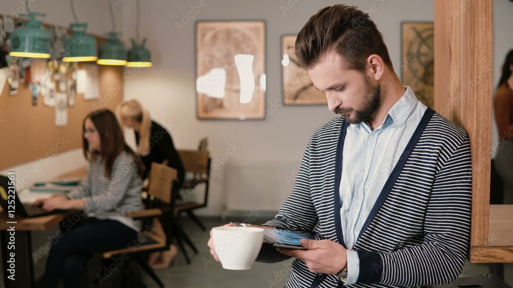 young handsome bearded man uses touchscreen tablet and drinking coffee in the modern startup office. young handsome bearded man uses touchscreen tablet and drinking coffee in the modern startup office.