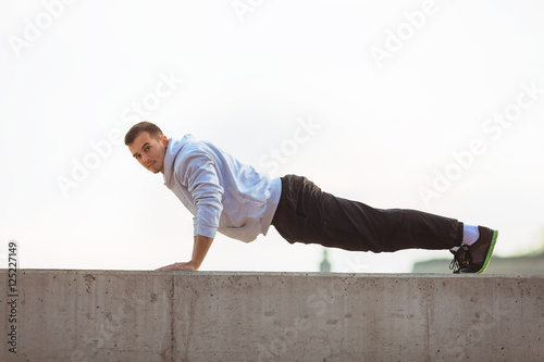 Attractive young man is exercising outdoors. He is doing push-ups on top of the wall.