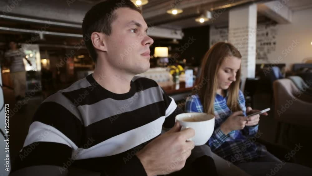 Young couple in cafe. Male drinking coffe while female using smartphone Young couple in cafe. Male drinking coffe while female using smartphone