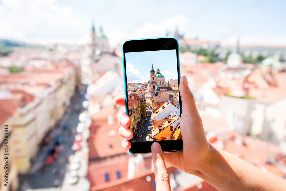 Naklejka premium Holding a smart phone with photo of the lesser town with saint Nicholas church in Prague city