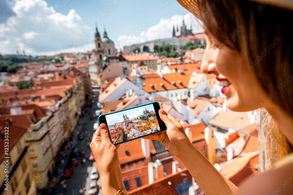 Fototapeta premium Young female tourist photographing with phone a beautiful cityscape of the old town of Prague