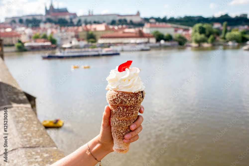 Naklejka premium Female hand holding traditional czech cookie called trdelnik on the river background in Prague.