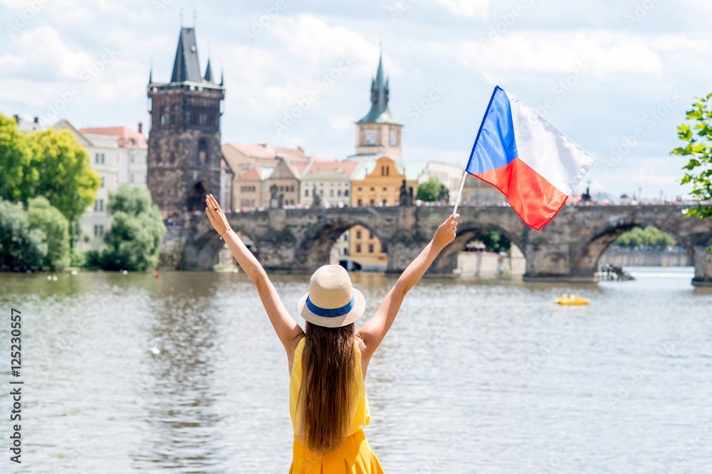 Fototapeta premium Młoda kobieta turystycznych z uniesionymi rękami, trzymając czeską flagę na tle starego miasta w Pradze.