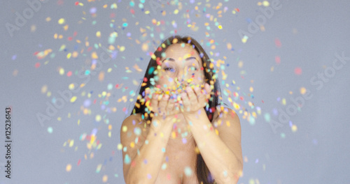 Young woman blowing colorful New Year confetti off the palms of her hands as she celebrates the holiday season photo