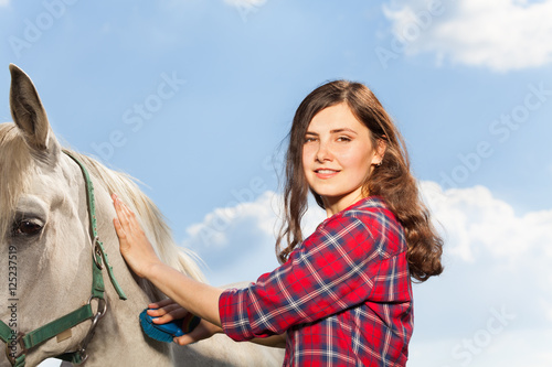 Portrait of young woman brushing a beautiful horse