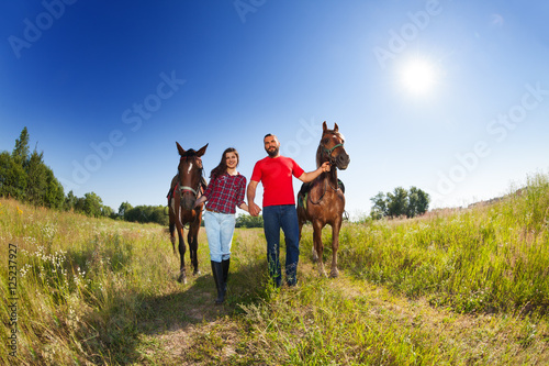 Loving couple walking with horses at sunny day