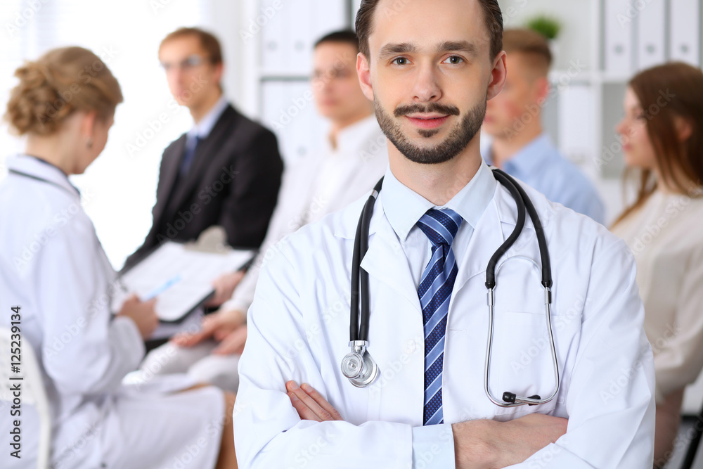 Friendly male doctor on the background doctor and many patients Friendly male doctor on the background doctor and many patients