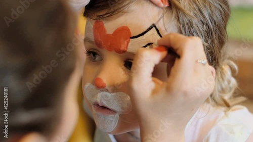 Little girl get painted face as a cat for a carnival