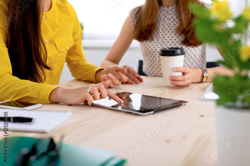 Two business woman or friends are talking and using tablet computer