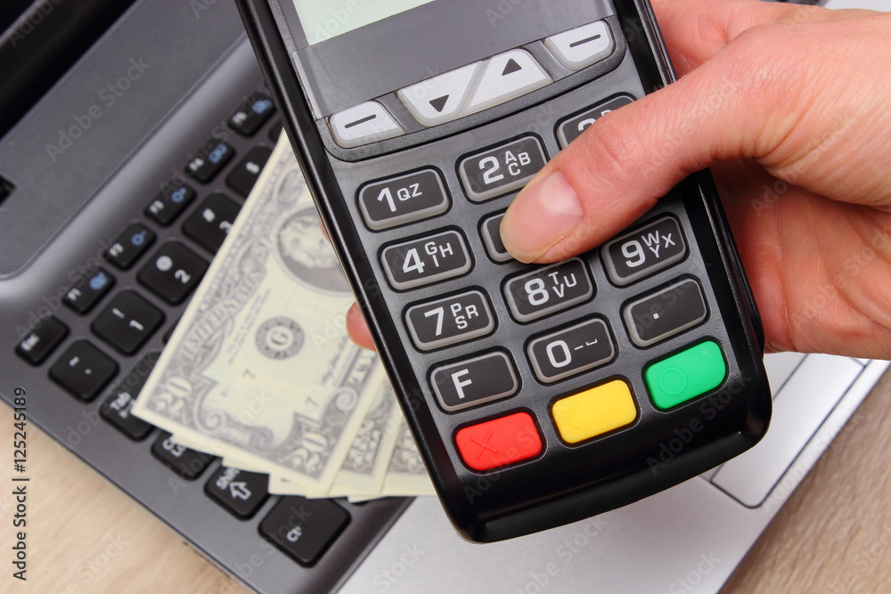 Hand of woman using payment terminal, currencies dollar on laptop in background Hand of woman using payment terminal, currencies dollar on laptop in background