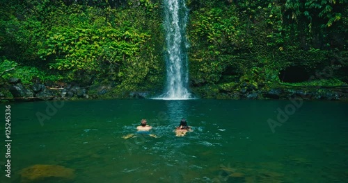 Attractive adventurous young couple swimming to beautiful waterfall