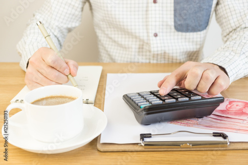 A man counting the money and making notes with a cup of coffee on the table