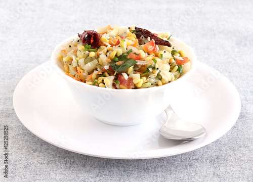 Kosambari, a traditional and popular, south Indian salad made from split mung bean, lentil, cucumber and other items, in a bowl on a plate with a steel spoon.