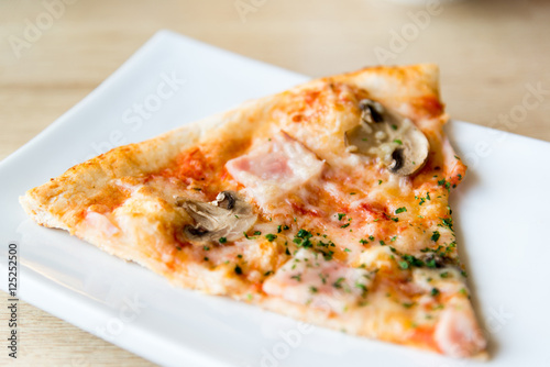 piece of pizza with mushrooms and ham on plate