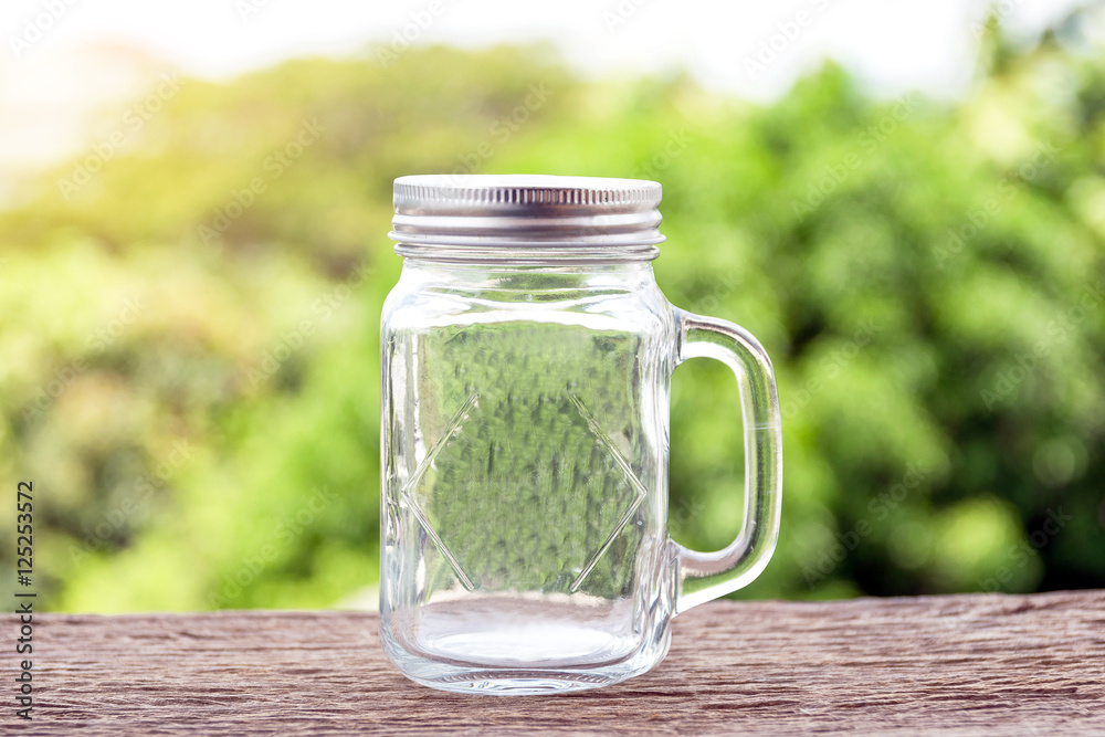 A glass jar with handle for drinks on wooden floor with green nature background. A glass jar with handle for drinks on wooden floor with green nature background.
