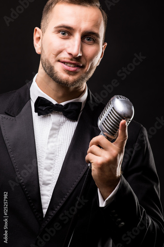 Handsome Man in suit singing with the microphone and smile. Isolated on black background. Showman concept.