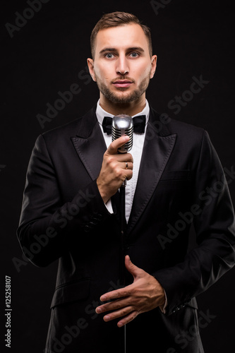 Handsome Man in suit singing with the microphone and smile. Isolated on black background. Showman concept.