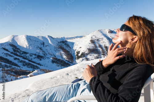 femme assise dans la neige s'appliquant de la crème protectrice sur le visage