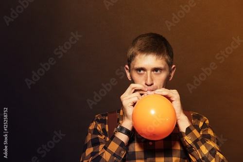 Tableau sur toile Young man puffing balloon on dark background