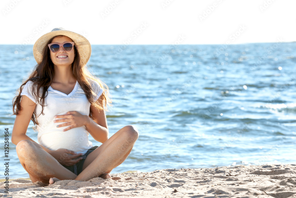 Young pregnant woman sitting on the beach
