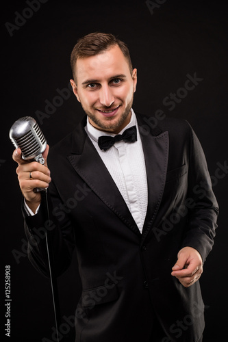 Portrait of handsome man sing on microphone on black background. Singer concept.