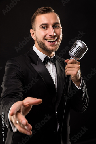 Portrait of handsome man sing on microphone on black background. Singer concept.