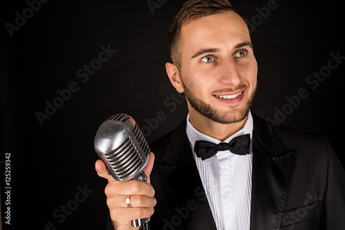 Portrait of handsome man sing on microphone on black background. Singer concept.