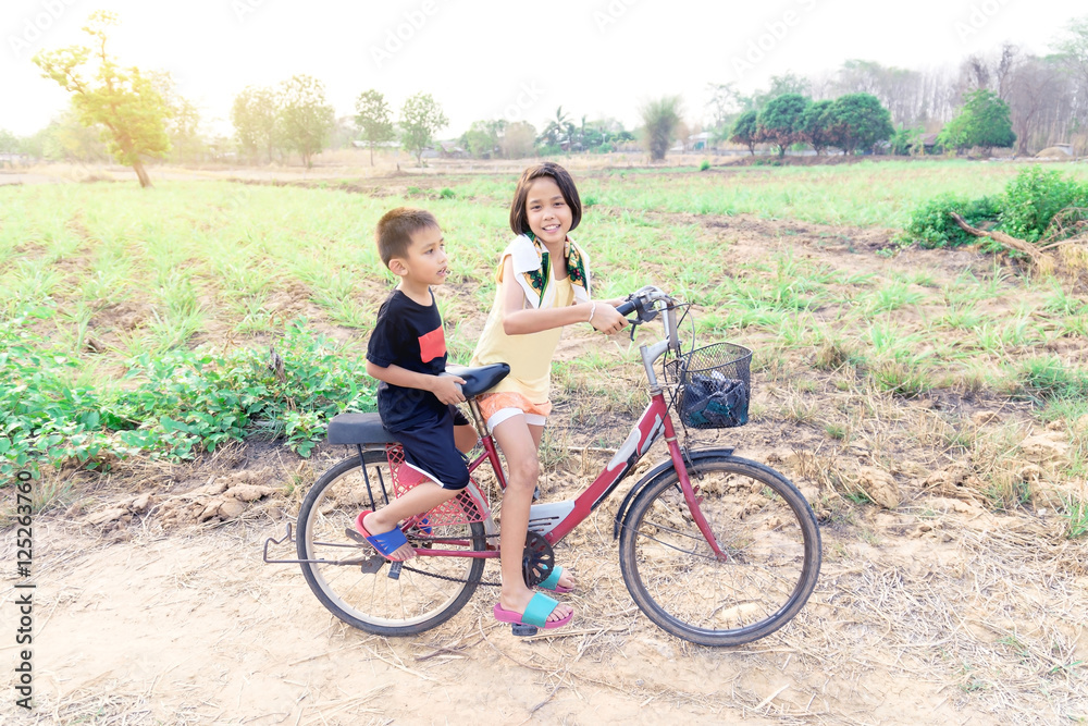 Sister and brother were riding a bicycle in the field.