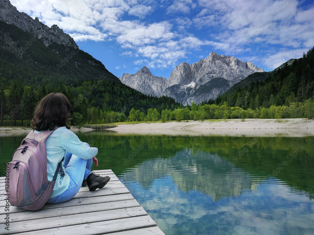 View of the Julian Alps with girl sitting on pier in Slovenia