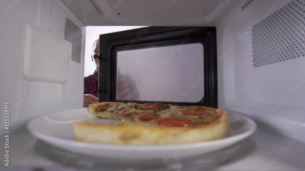 Reheating leftover pizza in the microwave. Young girl opens the door