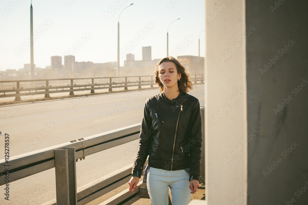 girl goes on road bridge. lonely young woman in black Leather jacket autumn, walking over the bridge which goes transport. girl goes on road bridge. lonely young woman in black Leather jacket autumn, walking over the bridge which goes transport.