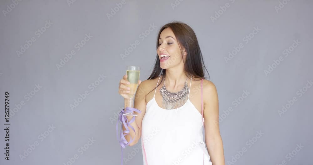 Happy young woman partying at New Year sipping from a glass of champagne as she holds a bunch of party streamers aloft in the other