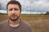 Portrait of adult strong man with beard at autumn meadow, energy pylons on background