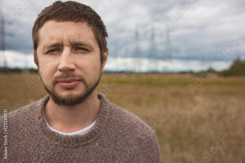 Portrait of adult strong man with beard at autumn meadow, energy pylons on background