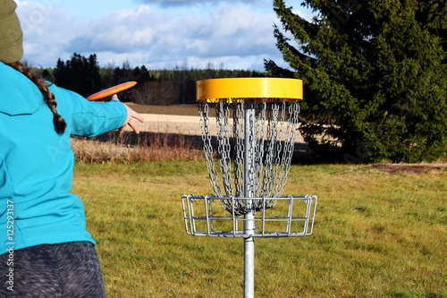Young woman throwing disc to target on disc golf course.