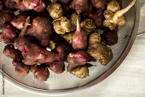 Fresh natural Jerusalem artichokes or sunchokes in a metal colander with a brown wood background