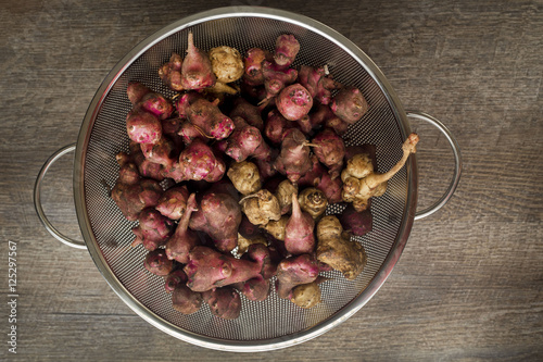 Fresh natural Jerusalem artichokes or sunchokes in a metal colander with a brown wood background photo