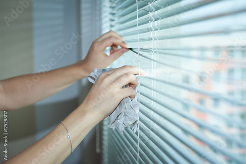 Hand of young woman cleaning blinds by cloth; housework (vignett photo