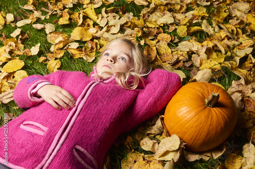 Child cute blond girl lying in autumn leaves with pumpkin.   © Petr Bonek