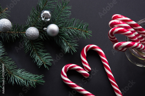 Christmas candy cane with silver evening balls and green fir tree on black background. Christmas concept. Top view and copy space, close up.