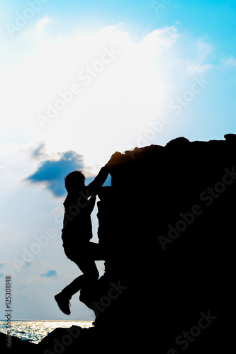 Young man climbing vertical cliff with sunset on ocean