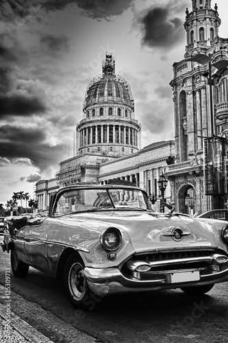 Black and white image of Havana street with vintage car and Capi
