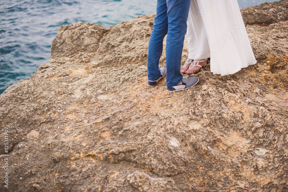 Romantic date near the sea. Young stylish caucasian couple standing side by side on a rock above the water. Romantic date near the sea. Young stylish caucasian couple standing side by side on a rock above the water.
