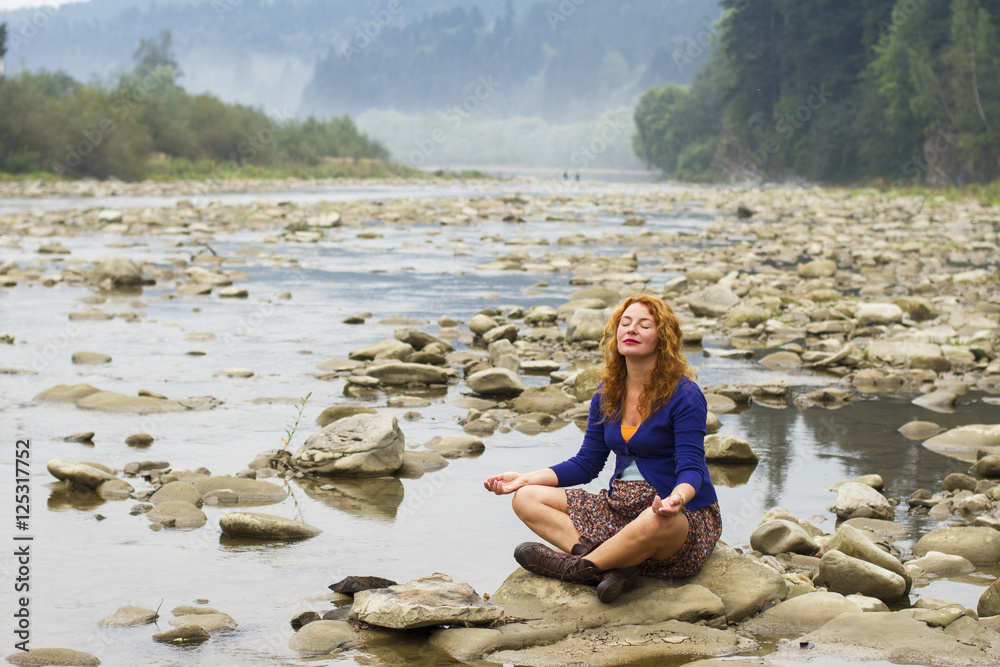 woman meditating sitting on stone in quiet location