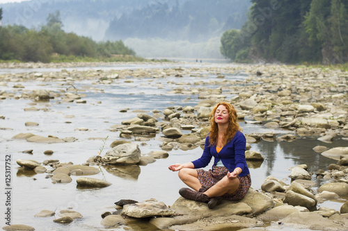 woman meditating sitting on stone in quiet location © kavardakova